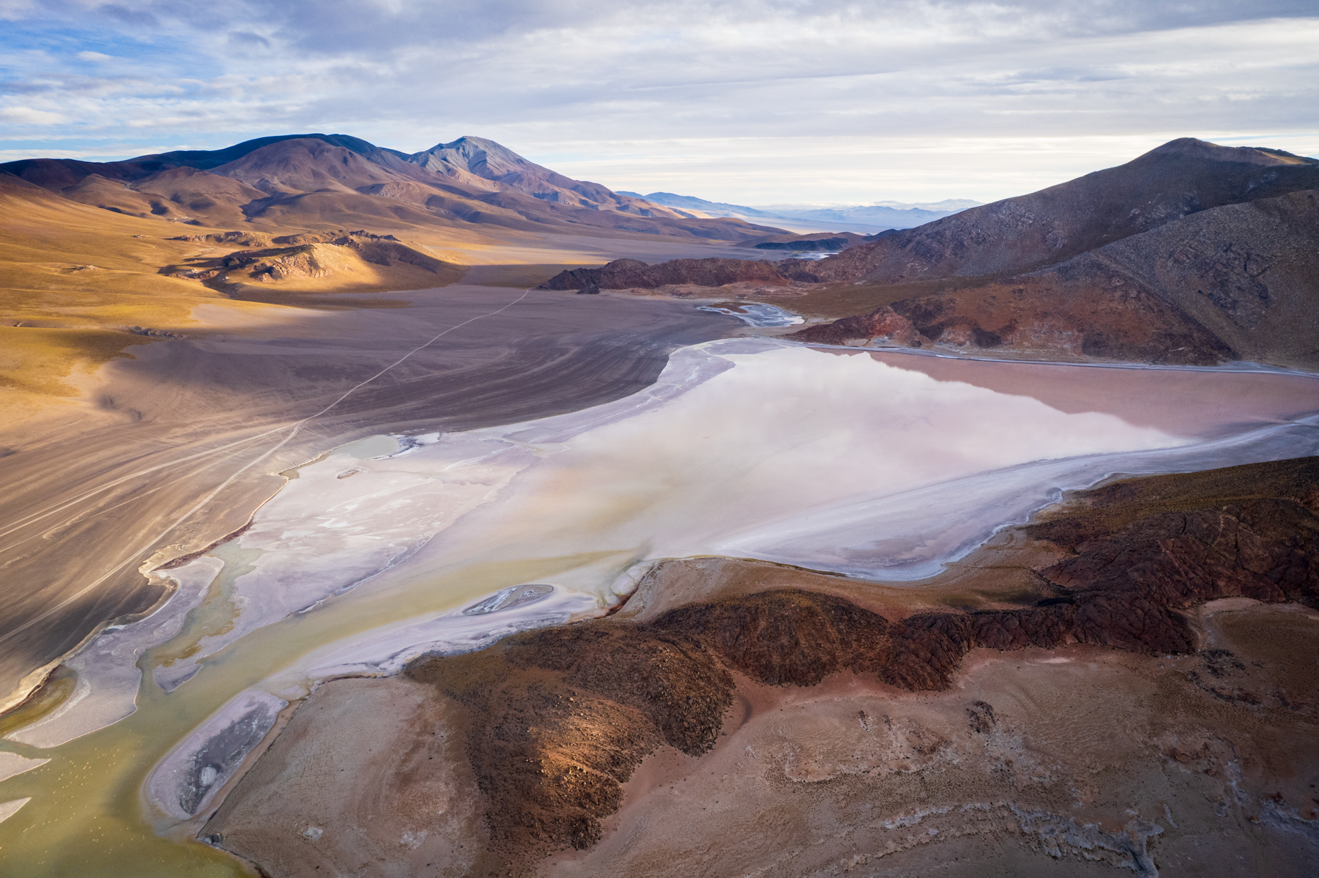 Weite Salzlagune in der argentinischen Puna mit farbigen Wasserflächen und kargen Vulkanbergen.
